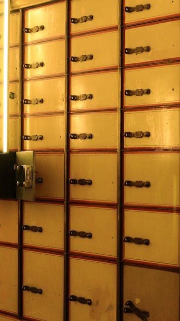 A close-up view of multiple vintage wooden storage lockers with small metal handles arranged in vertical columns, mounted on a wall in an indoor setting with warm lighting. The lockers are painted in a light beige or cream colour with red metal framing and appear to be part of a secure storage system, possibly used for storing valuables or personal belongings during a house relocation. The image focuses on the lockers' uniform arrangement and details such as the locking mechanisms and hinges, with a small metal safe box visible in the lower left corner. This setting reflects a secure environment suitable for storing fragile or antique items during furniture transport, which Man with Van Holborn might facilitate as part of their professional removals and packing services for home relocation involving bulky or valuable objects.